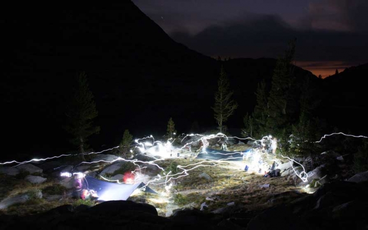 At a campsite, a time lapse of headlamp movement leaves the white trails of light throughout the camp.